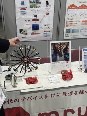 A Ferris wheel-style robot on a table with some small red keypads and signage explaining that they run PicoRuby/PRK firmware.