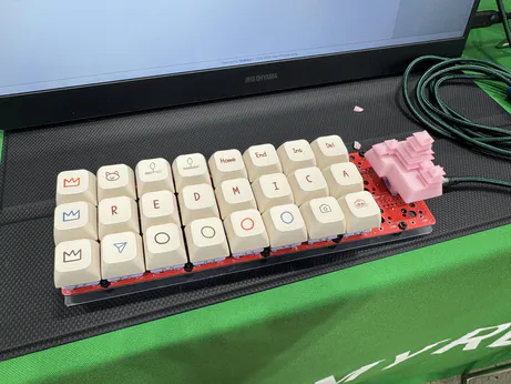 A custom orthographic keyboard with 3 rows and 8 columns. The keys across the middle read REDMICA and there is a pink key shaped like a Japanese castle on the right hand side.